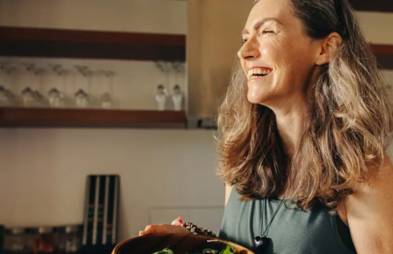 Mulher sorrindo em uma cozinha, com um prato montado em primeiro plano
