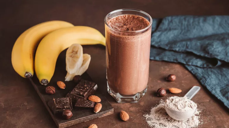 Shake proteico de chocolate ao lado de bananas, amêndoas, aveia e chocolate em pó